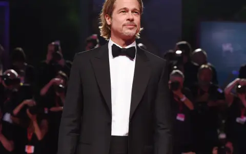 Brad Pitt looking dapper in a classic tuxedo with a black cummerbund and bow tie, posing for photographers.