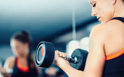 Frau hebt Hantel. Die Frage, wieviel kg darf eine Frau heben arbeitsrecht, ist hier nicht relevant, da es um Fitness geht.