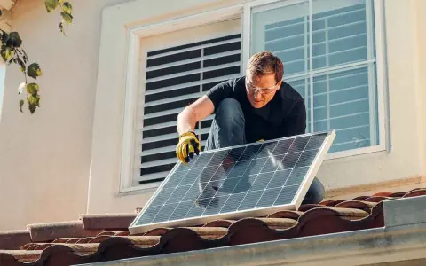 Instalación de placas solares en comunidad de vecinos. Un hombre con guantes y gafas de seguridad coloca un panel solar en un tejado.