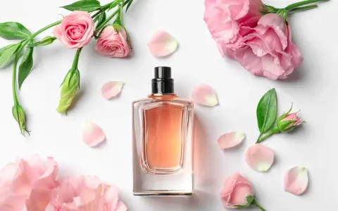 Elegancka butelka perfum z delikatnym, różowym płynem, otoczona pąkami i płatkami róż. Zapach jak słodka jeżyna.