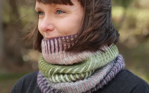 Woman wearing a colorful knitted cowl in shades of green, pink, and purple.