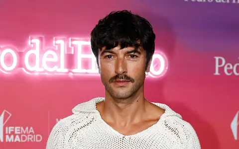 Hombre con un estiloso bigote, perfecto para Movember, luce un jersey blanco de punto.