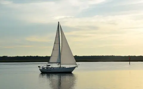 Un voilier blanc navigue sur une eau calme, ses voiles gonflées par le vent. La composition du bateau, avec la ligne d'horizon et le ciel doux, crée une scène paisible.