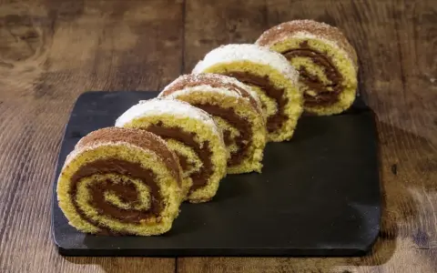 Fette di rotolo alla nutella cosparse di zucchero a velo e cacao, su una lavagna scura, pronte per essere gustate.