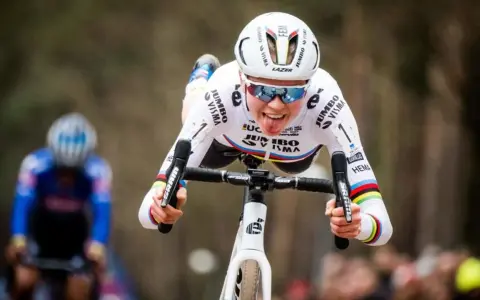 Fem van Empel zeigt Zunge beim Radrennen, trägt weißes Trikot mit Jumbo Visma Logo.