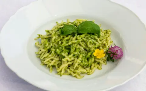 Pasta al pesto con hojas de albahaca fresca y flores comestibles.