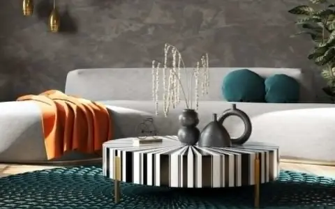 Nowoczesny salon w stylu feng shui z szarą kanapą, pomarańczowym kocem, czarno-białym stolikiem i turkusową podłogą.