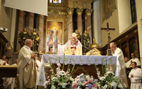 Uroczysta msza święta w kościele. Kapłan podnosi hostię, symbolizując piękna modlitwę do Boga. W tle złote zdobienia i obrazy.