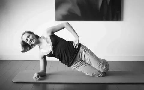 Femme souriante en plein gainage latéral sur un tapis de yoga.