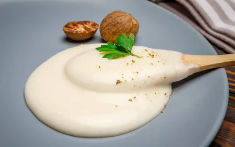 Krämig bechamelsås på en tallrik med muskotnötter och persilja. Perfekt för ditt bechamelsås recept.