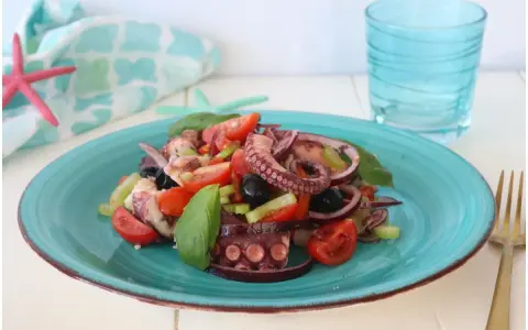 Un invitante polpo alla catalana su un piatto turchese, con pomodorini, olive e basilico. Fresco e saporito.