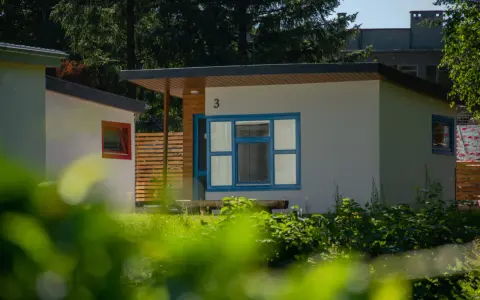 Nowoczesne domki letniskowe w osadzie Chmielaki. Jasne ściany, niebieskie okna i drewniane elementy tworzą przytulną atmosferę.