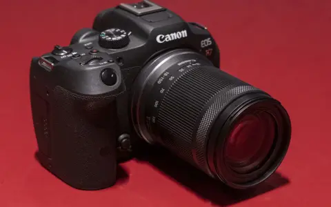 Appareil photo noir Canon EOS R7 avec objectif 18-150 mm, posé sur un fond rouge vif.