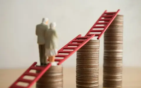 Figurki starszej pary stoją na stosach monet, połączonych czerwoną drabiną. Symbolizuje to nowe zasady przejścia na emeryturę i drogę do finansowej stabilności.