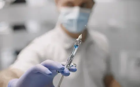 Dentysta w masce i rękawiczkach trzyma strzykawkę do znieczulenia nasiękowego.