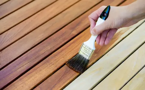 Application d'une lasure sur des lattes de bois. La différence entre lasure et peinture est visible : la lasure laisse le grain du bois apparent.