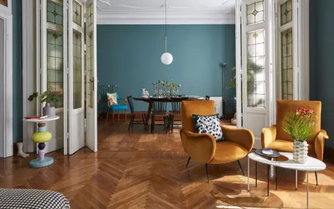 Un soggiorno che unisce con successo arredamento classico e moderno: sedie in velluto ocra, tavolino di design e porte antiche con vetri colorati.