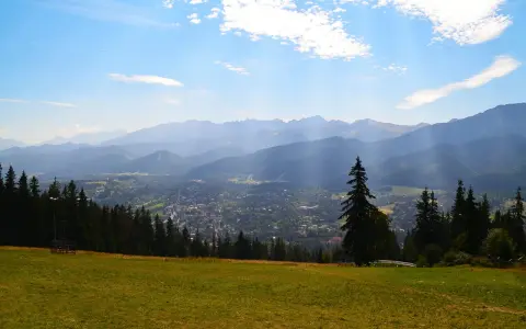 Widok z Gubałówki na Butorowy Wierch i Tatry. Słoneczny dzień, chmury na niebie.