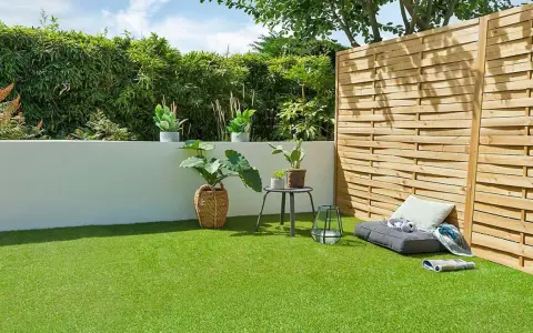 Terraza con césped artificial verde vibrante, plantas en macetas, un banco y una valla de madera.