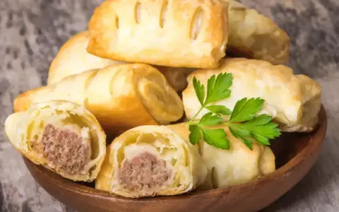 Stos pieczonego ciasta francuskiego z kiełbaską w środku, ozdobione natką pietruszki.