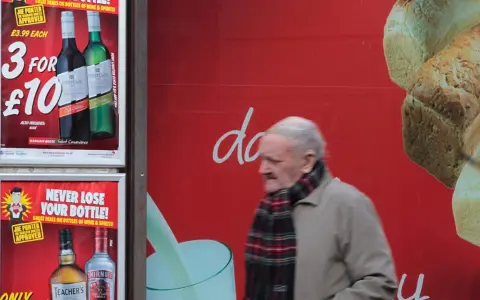 Starszy mężczyzna mija reklamę z promocją na alkohol. Włochy ceny alkoholu są atrakcyjne.