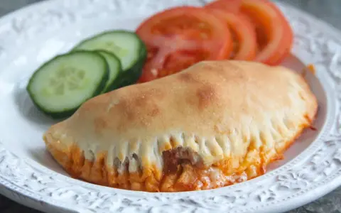 En gyllene pirog med ost och tomatsås, serverad med gurka och tomat. Ett perfekt piroger recept för en snabb måltid.