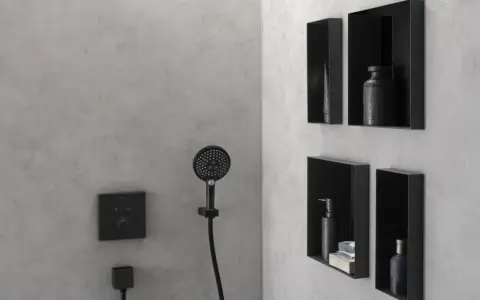 Nowoczesna półka w prysznicu z czarnymi, wbudowanymi schowkami na kosmetyki. Obok słuchawka prysznicowa i panel sterowania.
