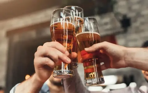 Trzy ręce unoszą kieliszki ze złotym piwem, tworząc toast. Każde piwo w szklance wygląda apetycznie.
