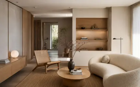 Salón de **estilo Japandi** con sofá curvo, silla de ratán, mesa de centro de madera y estanterías empotradas.