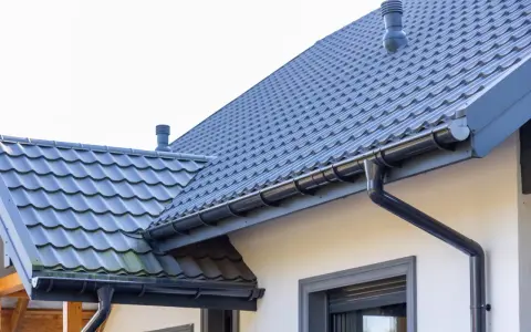 Szary dach z dachówki ceramicznej, rynny i komin. Sprawdź, jaka jest dachówka ceramiczna cena za m2.