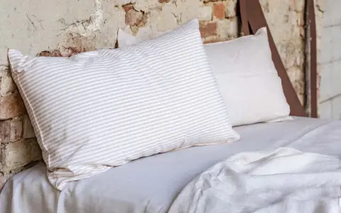 Cuscini a righe e tinta unita su un letto coperto da lenzuola di lino. Le caratteristiche del linone tessuto sono evidenti nella texture naturale.