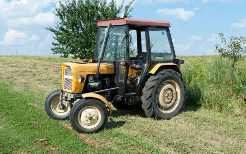 Żółty Ursus C-360 na łące. Pytanie o to, ile oleju do filtra powietrza C-360, jest kluczowe dla jego sprawnej pracy.