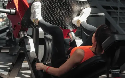 Kobieta ćwiczy na maszynie do wyciskania nóg, wykonując ćwiczenie push pull legs.
