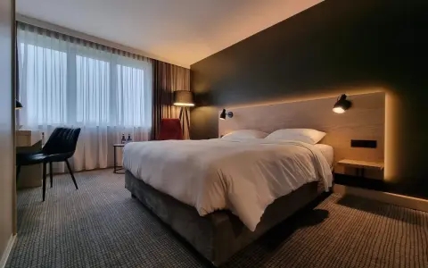 Przytulny pokój w Park Inn Papenburg: wygodne łóżko, designerskie lampy i okna z zasłonami.