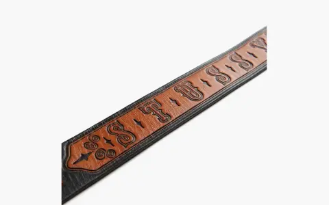 Cintura in pelle marrone con logo Stussy inciso e dettagli decorativi.