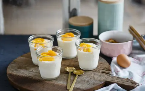 Vier Gläser mit cremigem Dessert, garniert mit Orangenspalten, ideal für Cointreau Rezepte. Zwei goldene Löffel liegen daneben.