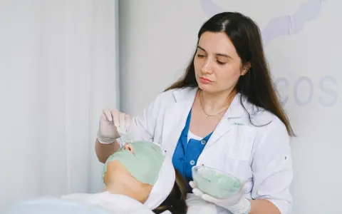 Dermatolog nakłada zieloną maskę na twarz pacjentki.