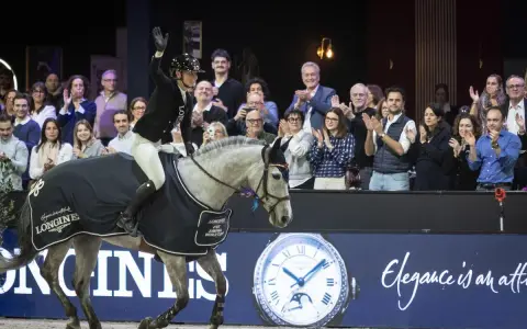 Cavalier(e) saluant la foule, son cheval gris couvert d'une cape aux couleurs de la Longines FEI Jumping World Cup.