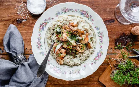 En tallrik med lyxig risotto toppad med räkor och svamp, serverad på ett vackert mönstrat fat.