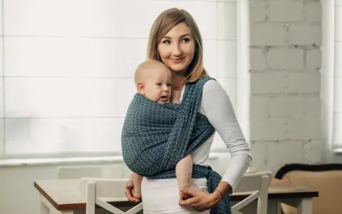Uśmiechnięta mama nosi dziecko w chuście tkanej, która zapewnia komfort i bezpieczeństwo.
