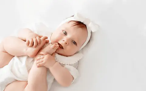 La bebé Cora, con su diadema de lazo blanco, juega con sus pies.