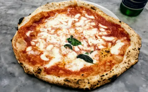 Pyszna pizza napoletana z rozpływającym się serem mozzarella i aromatycznym sosem pomidorowym, ozdobiona świeżą bazylią.