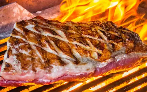 Jugosa viande de kobe a la parrilla, con marcas doradas y llamas naranjas danzando alrededor.