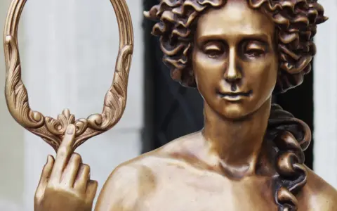 Bronzestatue der Aphrodite, die einen verzierten Spiegel hält. Ihr lockiges Haar und ihr sanfter Blick unterstreichen ihr klassisches Aphrodite-Aussehen.