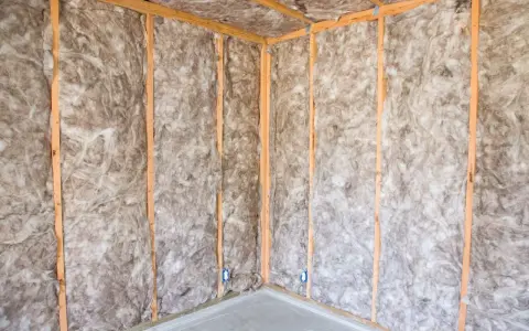 Coin d'une pièce en construction, murs et plafond recouverts d'isolation ouate de cellulose, structure en bois visible.