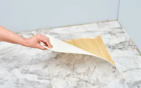 Mano retirando capa de vinilo del suelo. Un paso clave para saber como quitar pintura de caucho del suelo.