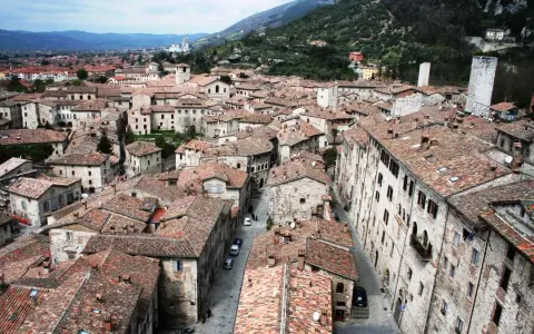 Panoramica di tetti rossi e antichi edifici in pietra, con torri medievali che svettano. Un paesaggio che ricorda l'Umbria, tra Assisi e Gubbio.