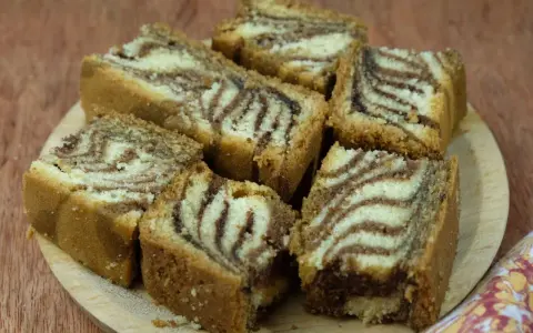 Kawałki ciasta zebra ułożone na drewnianej desce, z charakterystycznymi pasami jasnego i ciemnego ciasta.