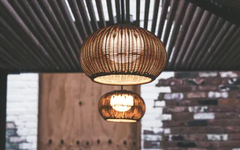 Dos lámparas de mimbre esféricas cuelgan bajo un techo de listones. La luz cálida que emiten crea un ambiente acogedor, con unos lumenes por m2 perfectos para relajarse.