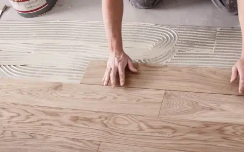 Hände legen Holzplanken auf Kleber, um den Boden zu verlegen.